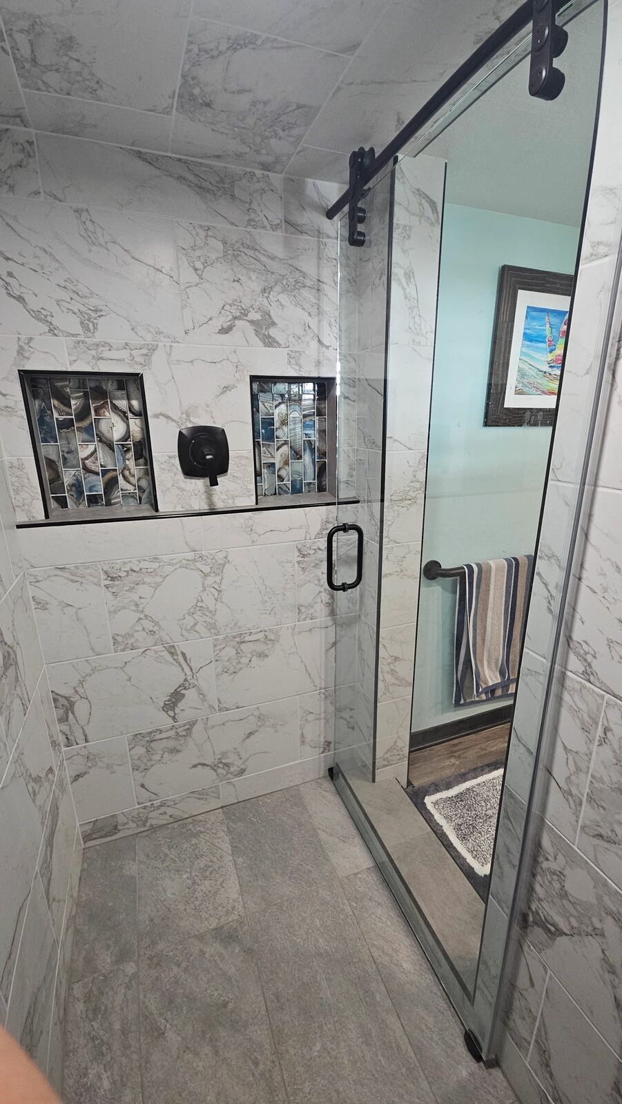 A marble-look shower with a black-framed glass door and recessed niche