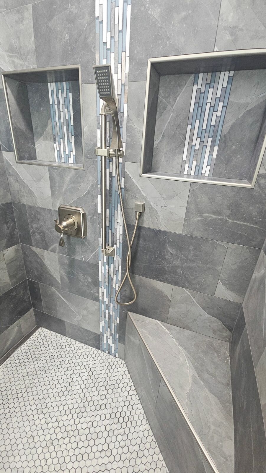 A walk-in shower with gray tile and a glass mosaic accent strip