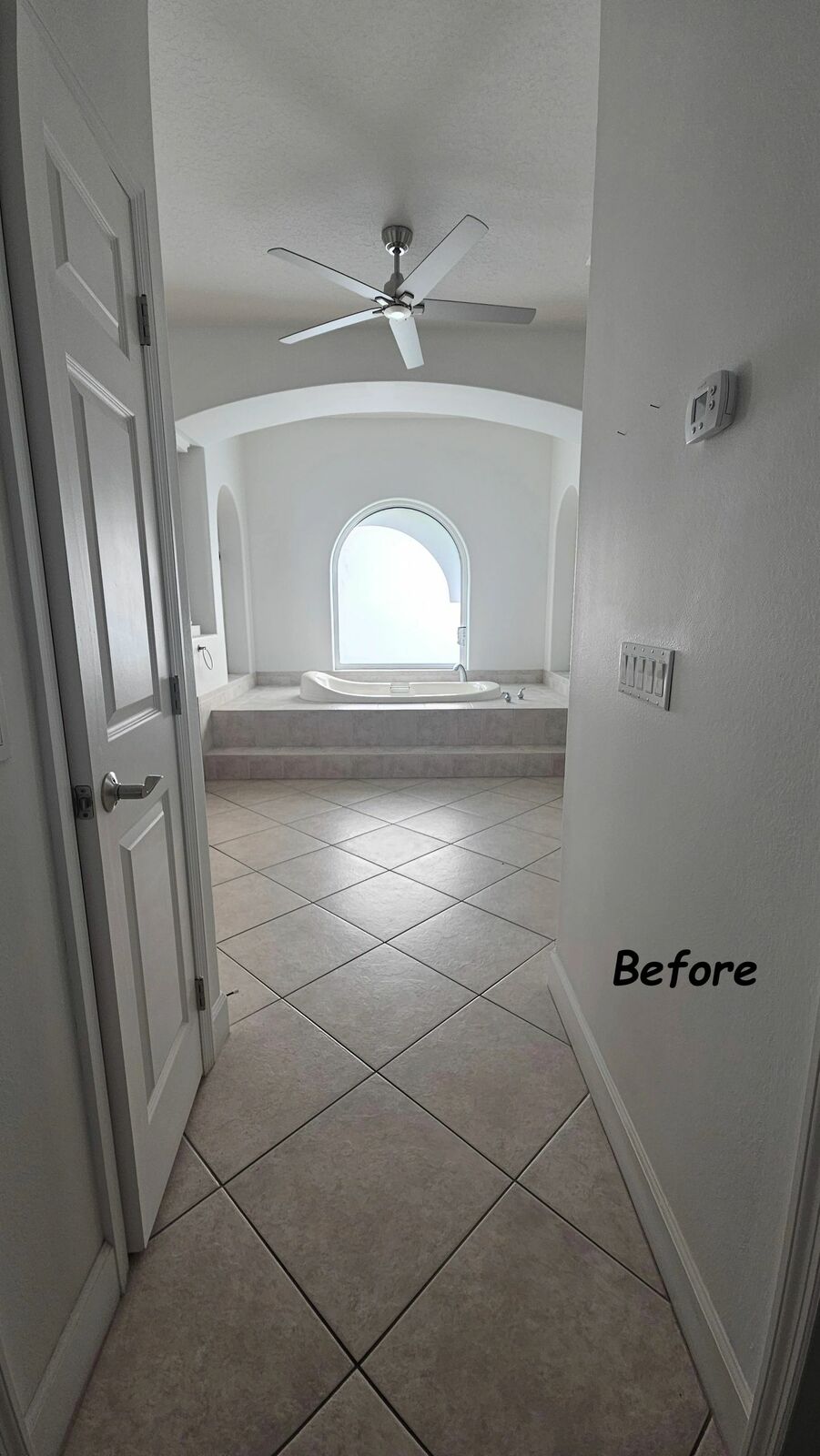 The master bath before: beige tile floors and an arched window over a step-up tub